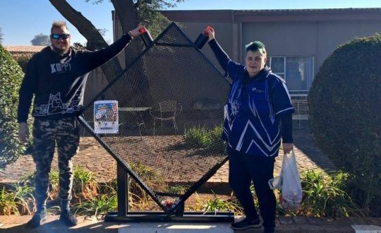 A photo of Gerda together with Anton on the frame he built to hold the bottle top doantions